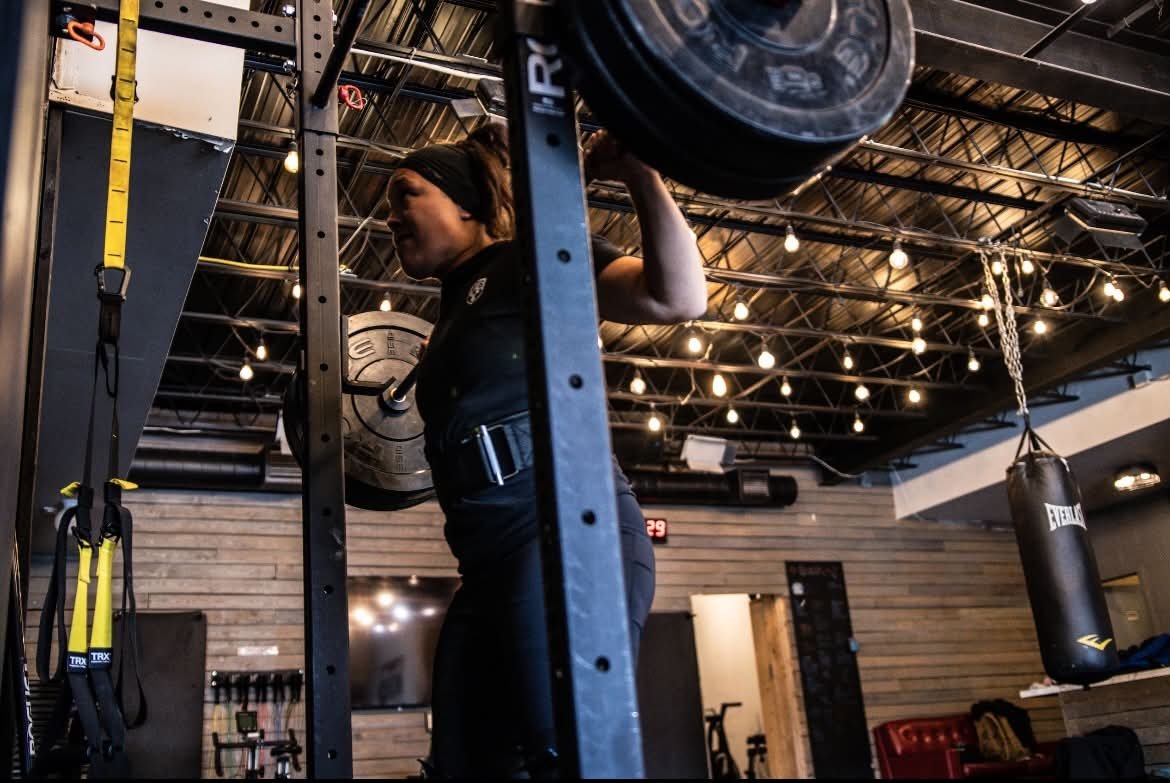 Coach JJ under a loaded barbell in a squat rack